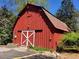 Exterior of a rustic red barn featuring white doors and detailed trim, surrounded by greenery at 605 Ga 120 Hwy, Roswell, GA 30075