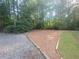 View of a spacious driveway lined with trees, gravel, and an open area at 605 Ga 120 Hwy, Roswell, GA 30075