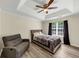 This bedroom offers a tray ceiling, ceiling fan, chair, a gray bed and wood-look flooring at 2880 Field Spring Dr, Lithonia, GA 30058