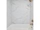 White tub and shower combo with elegant white marble-style tile and sleek gold fixtures at 4191 Hosch Reserve Dr, Buford, GA 30519