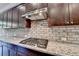 Close-up of stovetop with stainless steel range hood and granite countertops with brick backsplash at 12095 Cameron Dr, Duluth, GA 30097