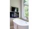 Bright bathroom with a soaking tub with TV, glass shower, and a large arched window with natural light at 818 Forest Path Ln, Alpharetta, GA 30022