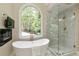 A luxurious bathroom featuring a soaking tub, glass shower, and large arched window with natural light at 818 Forest Path Ln, Alpharetta, GA 30022