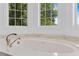 Close up on a garden tub with marble surround, elegant faucet and large windows for natural light at 3030 Berry Rd, Loganville, GA 30052