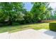 A large backyard showcasing a concrete patio, lush green grass, mature trees and landscaping, and a privacy fence at 690 Glenforest Rd, Sandy Springs, GA 30328