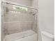 Modern bathroom featuring gray tiled walls, a bathtub with glass doors, and a window at 435 Webb Dr, Norcross, GA 30071