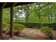View from the covered patio into the fenced backyard with mulched garden and mature trees at 385 Windy Pines Trl, Roswell, GA 30075