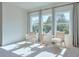 A seating area filled with natural sunlight, featuring two chairs, a small table, and tree views from three large windows at 3440 Carswell Bnd, Cumming, GA 30028