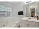 Bright bathroom with white cabinets, a bathtub, a window and a mounted TV at 1185 Charter Club Dr, Lawrenceville, GA 30043