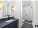 Hallway bathroom with a dark blue vanity, a bright gold sconce and a shower with modern black-trimmed door at 11530 Serenbe Ln, Chattahoochee Hills, GA 30268