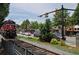 Exterior view of a train traveling along a street, commercial buildings, landscaping, and mature trees at 116 Via Roma, Woodstock, GA 30188