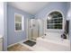 Ensuite bathroom with standalone tub, shower, and light-blue walls is brightened with two windows at 2759 Beddington Way, Suwanee, GA 30024