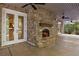 Covered outdoor patio with a stone fireplace, brick walls, outdoor lighting, ceiling fans and concrete flooring at 9179 Selborne Ln, Chattahoochee Hills, GA 30268
