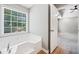 Bright bathroom featuring a soaking tub under a window and an open doorway leading to the bedroom at 5590 Princeton Oaks Dr, Sugar Hill, GA 30518