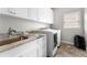 Well-lit laundry room with granite countertops, white cabinets, a stainless steel sink, and modern washer and dryer at 12980 Overlook Pass, Roswell, GA 30075