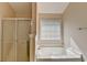 Bright bathroom featuring a bathtub, glass shower door, window with blinds and neutral colored walls at 1405 Bramlett Forest Trl, Lawrenceville, GA 30045