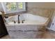 Bright bathroom featuring a corner bathtub surrounded by decorative neutral-toned tiles and a window at 621 Oakbourne Way, Woodstock, GA 30188