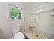 Bathroom with glass enclosed shower, built in bench, stone floor, tiled walls, toilet, and window at 3306 Emory Dr, Marietta, GA 30062