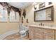 Bright bathroom featuring a single sink vanity with framed mirror, a window, and a toilet with cowboy boot decor at 878 Middle Fork Trl, Suwanee, GA 30024