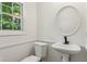 Well-lit half-bath featuring pedestal sink, round mirror, toilet, and a window at 3845 Pilgrim Mill Rd, Cumming, GA 30041
