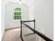 Upstairs hallway with arched window, neutral carpet, and staircase featuring white spindles and a black handrail at 3845 Pilgrim Mill Rd, Cumming, GA 30041