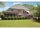 Expansive backyard featuring a brick house, covered deck, manicured lawn, patio with umbrellas, and a hot tub at 3235 Munsey Ct, Cumming, GA 30041