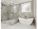 This primary bathroom features a luxurious tub, walk-in shower with glass door, and gray tiled walls at 2977 N Bogan Rd, Buford, GA 30519