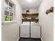 A well-lit laundry room featuring a washer and dryer set, stylish floating shelves, and a view to the outdoors at 6520 Glen Pond Trce, Cumming, GA 30028