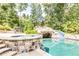 Backyard pool featuring a stone grotto with slide, surrounded by lush greenery and a stone patio with seating at 4090 Cooks Farm Nw Dr, Kennesaw, GA 30152