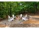 A stone fire pit with white Adirondack chairs, surrounded by a wooded area for outdoor gatherings at 6800 Wright Rd, Atlanta, GA 30328