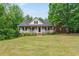 Charming home with a covered front porch, green lawn, and mature trees around the property at 418 Whisper Wood Way, Locust Grove, GA 30248