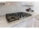 Close up view of marble countertops, gas range stovetop, white cabinets, and subway tile backsplash at 359 Alderwood Ln, Atlanta, GA 30328