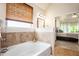 Bright bathroom with garden tub, tile surround, and an adjacent bedroom with a king bed at 6140 Stillwood Ln, Cumming, GA 30041