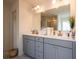 Bathroom with double sinks, a large mirror, and gray cabinets with gold hardware at 13568 Scenic Pkwy, Covington, GA 30014