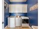 Bright laundry room with blue walls, modern washer and dryer, and white cabinets for organized storage solutions at 1963 Skybrooke Ln, Hoschton, GA 30548