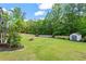 Beautiful backyard featuring a lush green lawn, a fire pit, mature trees, and a storage shed at 7493 Elderberry Dr, Douglasville, GA 30135