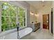 Bright bathroom featuring a soaking tub with black fixtures, gray vanity, and a large window overlooking lush greenery at 3599 Centerville Rosebud Rd, Snellville, GA 30039