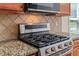Close-up of stainless steel gas range and granite countertops with tiled backsplash at 1125 Harvest Brook Way, Lawrenceville, GA 30043
