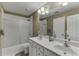 Bright bathroom featuring double sinks, white cabinetry, and a shower-tub combination with glass doors at 1563 Country Wood Dr, Hoschton, GA 30548