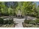 Outdoor brick fireplace with seating, surrounded by lush landscaping and mature trees at 3888 Peachtree Dunwoody Rd, Atlanta, GA 30342
