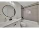 Modern bathroom features a round mirror, white vanity, gray textured tile, and tub with shower at 2328 Carnes Rd, Jonesboro, GA 30236