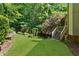 Backyard featuring a green lawn, landscaped garden beds, stairs to a deck, and privacy trees at 1477 Edenham Ln, Cumming, GA 30041
