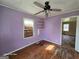 View of bedroom with peeling wood floors, light purple walls, white trim, and a three blade ceiling fan at 1243 Hill Nw St, Conyers, GA 30012