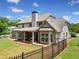 Beautiful home back exterior featuring a stone chimney, black fence, and covered patio space at 161 Archstone Sq, Mcdonough, GA 30253
