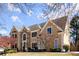Two-story home with manicured lawn, tan siding, stone accents, and dormer windows against a partly cloudy sky at 300 Morganshire Pl, Atlanta, GA 30350