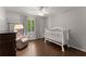 Cozy bedroom with hardwood floors, a white crib, and a comfortable armchair by the window at 4680 Brighton Lake Dr, Cumming, GA 30040