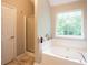 Bright bathroom featuring a soaking tub with a view, glass shower, and a white door at 1020 Travitine Trl, Loganville, GA 30052