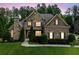 Evening view of brick home boasting manicured landscape, stone chimney, and inviting illuminated windows at 390 Scott Farm Dr, Powder Springs, GA 30127