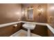 Elegant powder room featuring a pedestal sink, decorative mirror, and sconce lighting against warm brown walls at 5309 Ashley Trce, Atlanta, GA 30360
