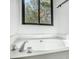 A relaxing, all-white soaking tub is situated under a black-framed window providing natural light at 267 Rocky Point Rd, Covington, GA 30014